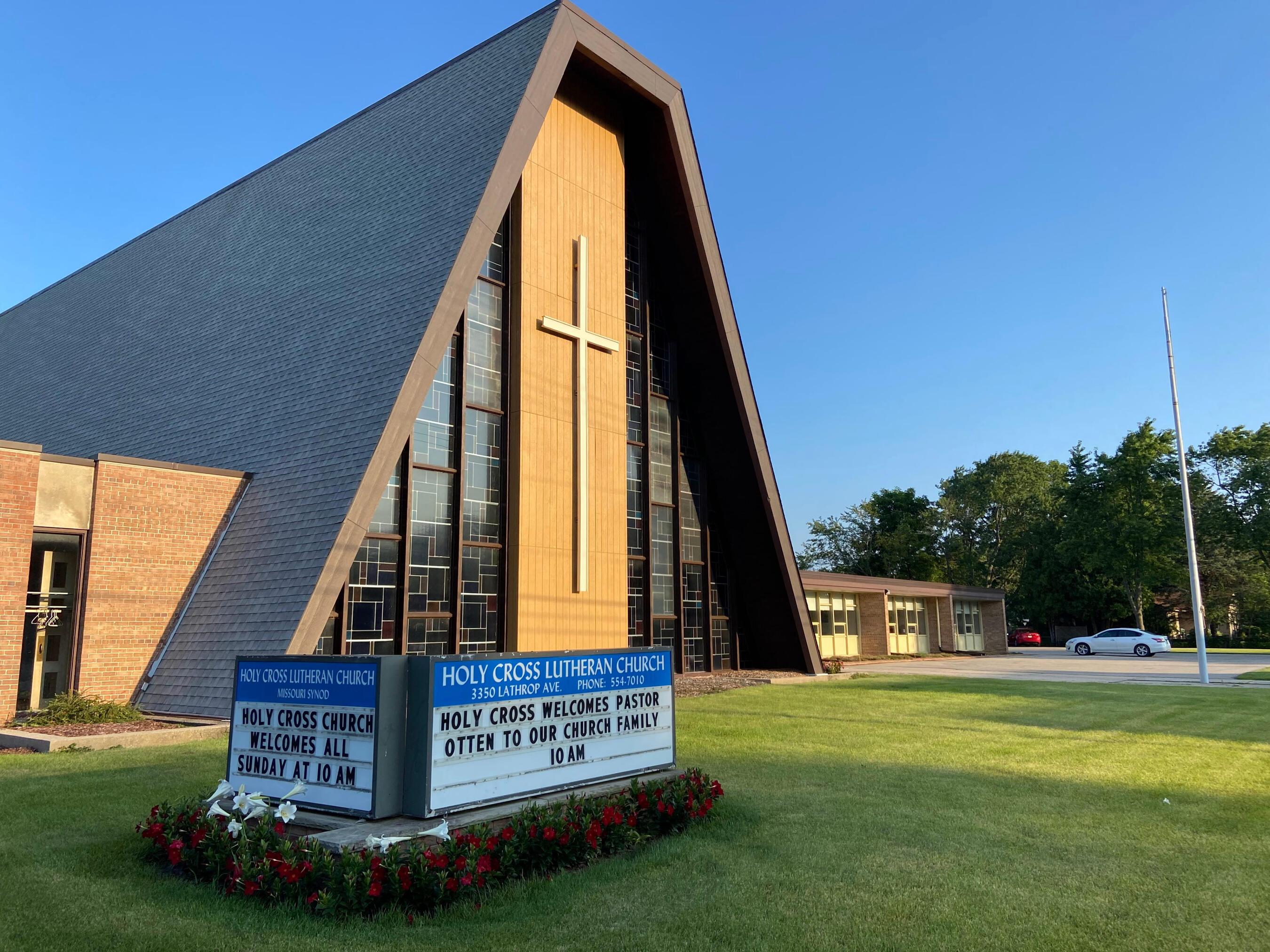 Holy Cross Lutheran Church in Racine, Wisonsin An exterior shot of Holy Cross Lutheran Church in Racine, Wisconsin. They have an A-frame roof, with stained glass on the left and right sides of the front, flanking a large cross in the middle. They have a sign out front welcoming Pastor Otten and his fam
