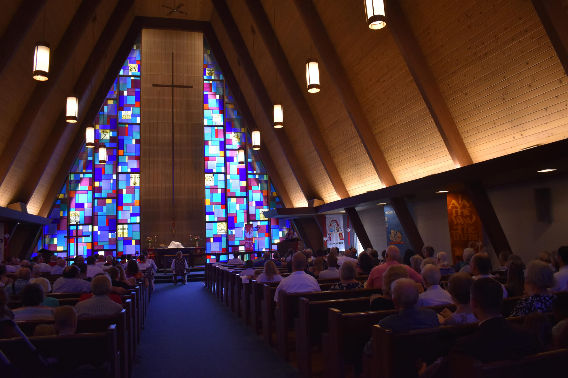 Pastor Luke Otten's installation at Holy Cross Lutheran Church in Racine, Wisconsin. The sanctuary at Holy Cross Lutheran Church in Racine, Wisconsin during a worship service. This is from the installment of Pastor Luke Otten. He sits in a chair at the center front of the nave. The church is full, with many decorative banners, and blue and